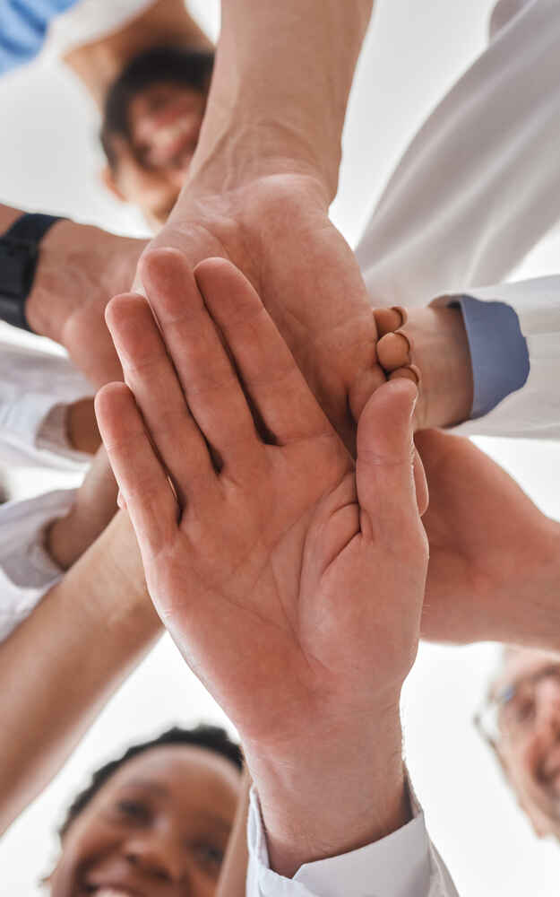 Group of physicians stacking hands together to represent teamwork