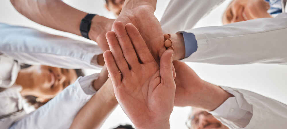 Group of physicians stacking hands together to represent teamwork